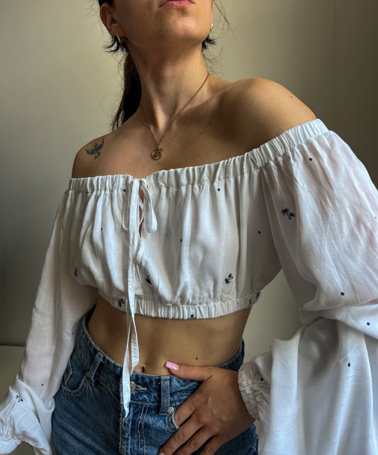 Person wearing a white off-shoulder top with blue jeans indoors.