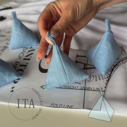 Hand holding a small blue fabric triangle sewing weight with sewing pattern paper in the background