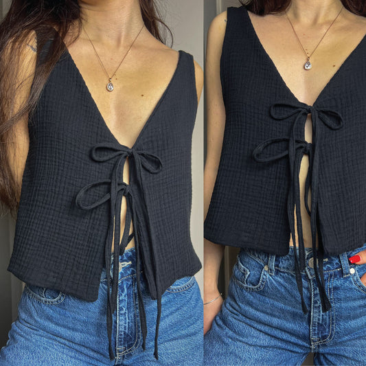 A sleeveless black textured knit top with a deep V-neck and front tie closure, shown on a model wearing blue jeans in a split-screen view.