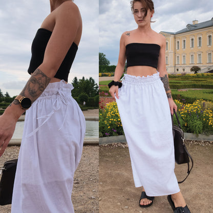 A woman modeling a white high-waisted linen skirt with a ruffled drawstring cinched waistband, paired with a black strapless tube top and black sandals, shown in a split outdoor portrait view.