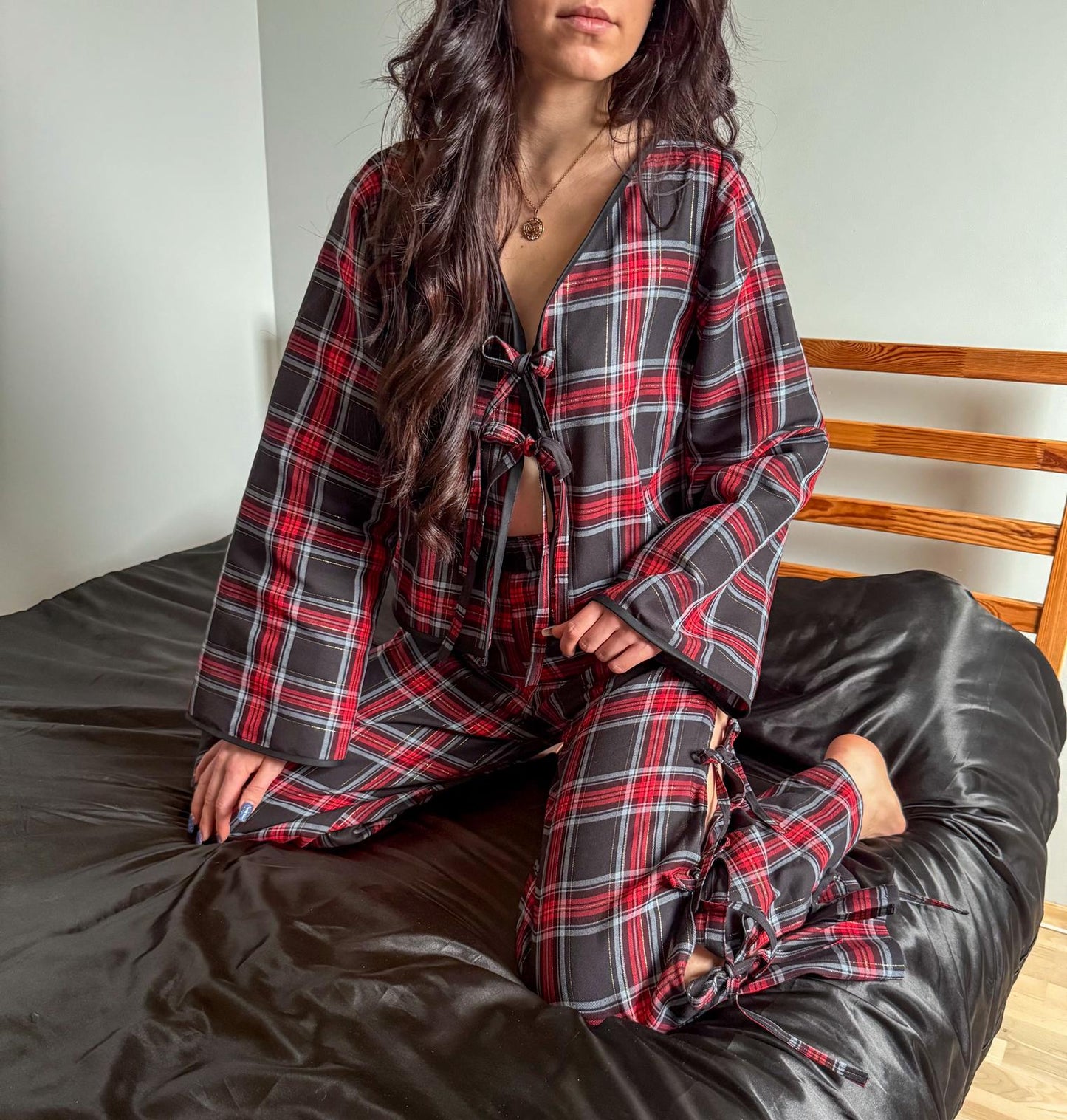 Model sitting on a bed wearing a red and black plaid cherry blouse with front ties and matching gingham pants with side ties made from a sewing pattern.