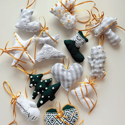 A collection of handmade Christmas fabric ornaments shaped like socks, hearts, stars, mittens, and Christmas trees, arranged on a light beige background. The ornaments feature white and gray gingham patterns, dark green velvet, white lace, gold ribbons, and small pearl embellishments.