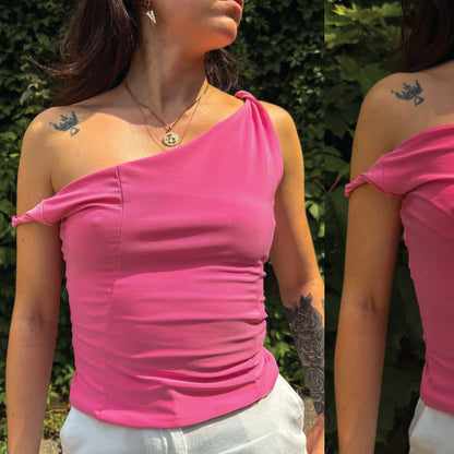 A woman wearing a bright pink one-shoulder ruched top, shown in a split view with front and back details against a green outdoor background.