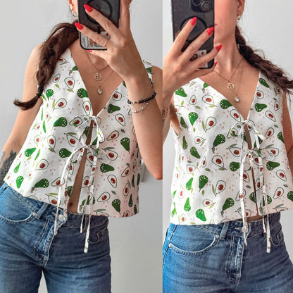 A split-screen mirror selfie showing a woman wearing a white sleeveless V-neck top with a green avocado print and tie-front detail, paired with blue jeans.