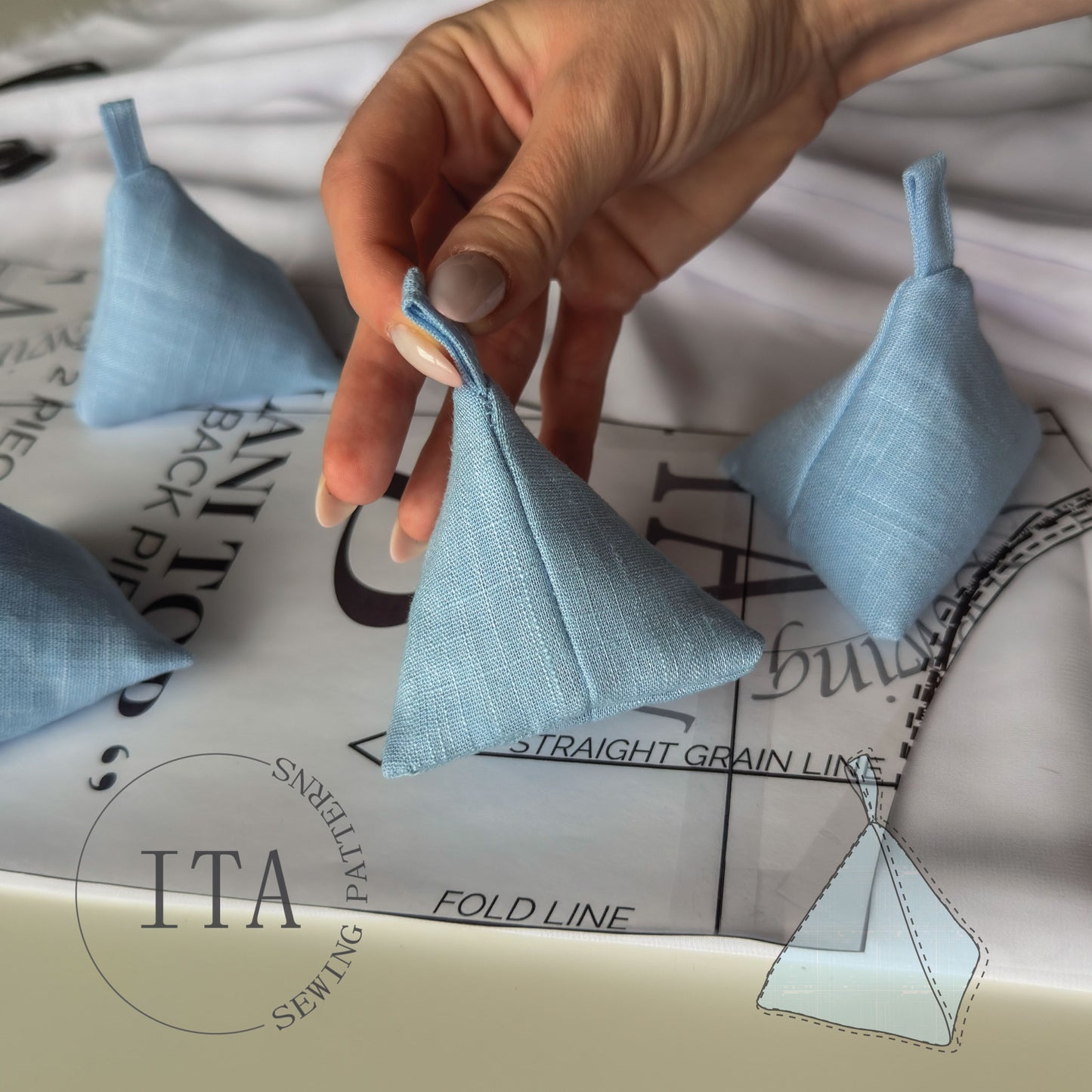 Hand holding a small blue fabric triangle sewing weight with sewing pattern paper in the background