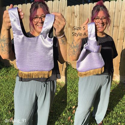 A woman outdoors in front of a wooden fence and grass holds up a lavender satin shoulder bag with fringe trim made with a beginner PDF pattern. The image shows two side-by-side views of the same bag, with text reading 'Size S Style A'.