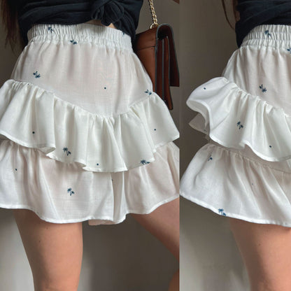 White tiered ruffle mini skirt with small blue floral embroidery, shown on a model from the side and back.