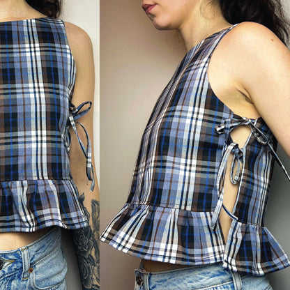A sleeveless plaid crop top with side tie details and a ruffled hem, shown on a model from both the back and side angles against a plain indoor background.