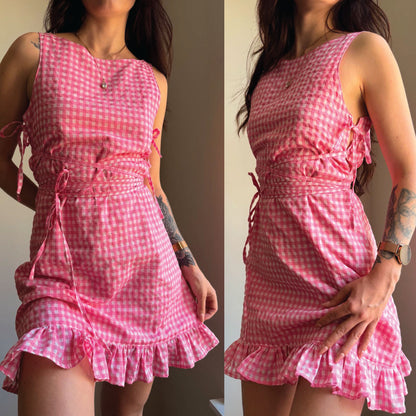 A pink and white gingham mini dress with a ruffled hem, side ties, and a gathered waist, shown in a split-screen front and back view on a model.