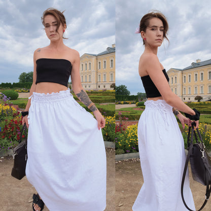 A split view of a woman outdoors wearing a black strapless tube top and a very wide white skirt, standing in front of a large historic building with manicured gardens. She is holding a black handbag.