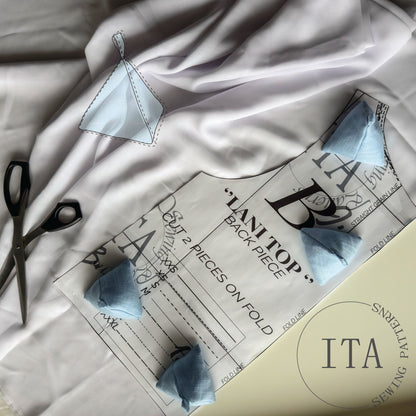 Sewing pattern with sewing weights  and scissors on a white surface. Ita sewing patterns logo. Baby blue sewing weights.