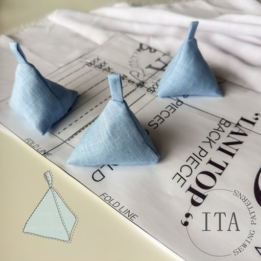 Blue triangular sewing weights on fabric piece and sewing pattern. Logo of ita sewing patterns in corner.