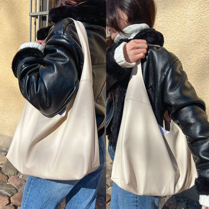 A person wearing a black faux-leather jacket with dark fur trim and a cream-colored slouchy shoulder bag, shown in a split view from the back and side against a beige stucco wall.