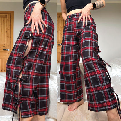A side-by-side comparison of a person wearing wide-leg plaid pants. The pants feature a red, black, and gray tartan pattern with unique side cutouts and black lace-up ties.