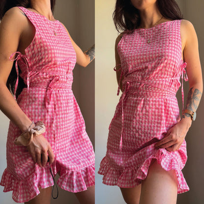 A sleeveless pink and white gingham mini dress with a tie waist and ruffled hem, shown in a side-by-side front and back view on a model.