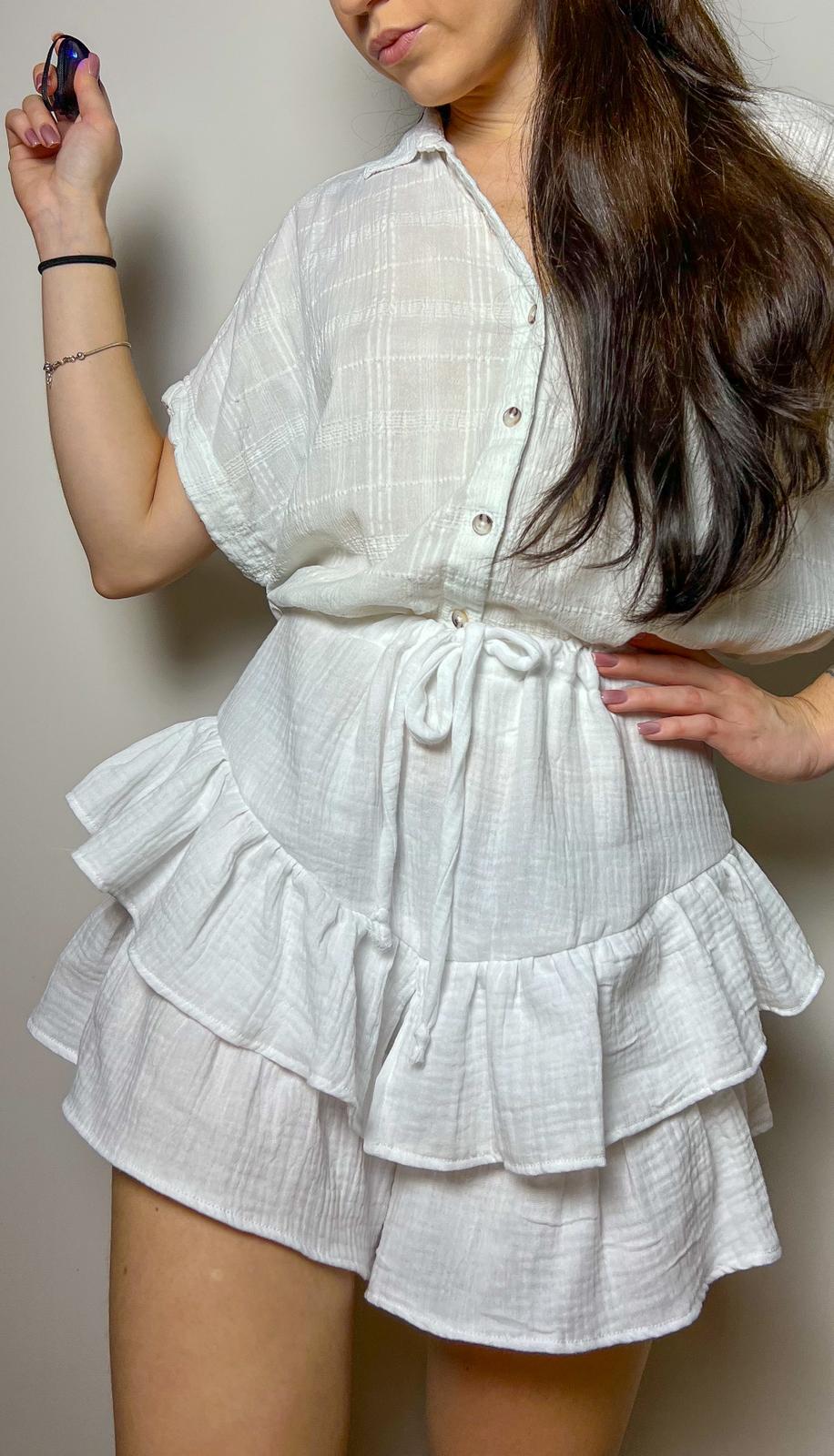 Woman wearing finished Velora shorts sewing pattern in white fabric with ruffled layers and tie waist, shown against a neutral background.